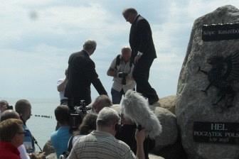 Grupa ludzi uczestniczy w odsłonięciu kopca Kaszubów na tle nieba.