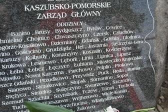 Granitowa tablica pamiątkowa z nazwiskami i wiązanką kwiatów na kopcu Kaszubów.