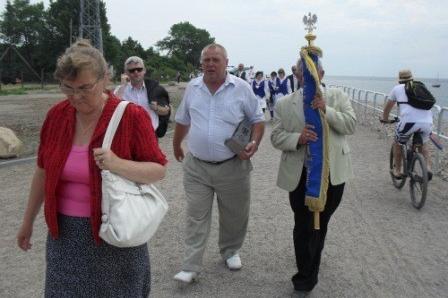 Grupa ludzi z kaszubską flagą maszeruje wzdłuż plaży na Helu podczas wydarzenia.
