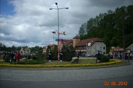 Żukowo 02.06.2012: ulica z latarniami, budynkami i zielenią pod zachmurzonym niebem.
