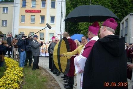 Biskupi pod parasolem, ludzie z tarczą, uroczystość 800-lecia Żukowa przy budynku.