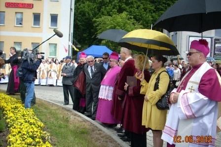 Duchowni i uczestnicy obchodów 800-lecia Żukowa pod parasolami podczas deszczowej uroczystości.