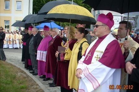 Biskupi i duchowni stoją w rzędzie, niektórzy pod parasolami, podczas obchodów 800-lecia Żukowa.