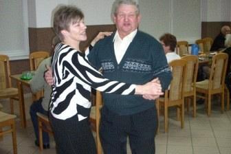 Uśmiechnięty mężczyzna w ciemnym stroju wręcza nagrodę młodszemu na Zabawie Andrzejkowej.