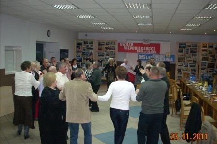Grupa dorosłych tańczy w kręgu, trzymając się za ręce, podczas Zabawy Andrzejkowej.