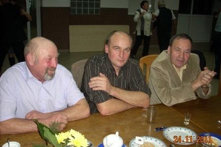 Trzech mężczyzn siedzi przy stole, rozmawiając na andrzejkowej zabawie.