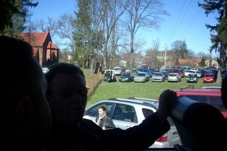 Uczestnicy targów ogrodniczych patrzą na parking pełen samochodów i wiosenny krajobraz.