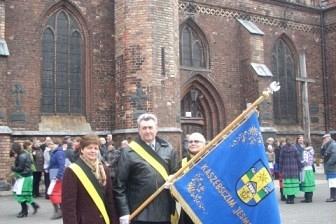 Uczestnicy Dnia Jedności Kaszubów niosą sztandar przed zabytkowym kościołem w Słupsku.