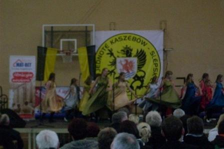 Koncert kaszubski w hali sportowej z zespołem na scenie i publicznością.