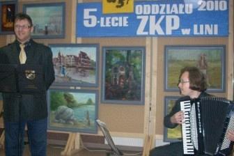 Dwóch mężczyzn na obchodach 5-lecia ZKP, jeden gra na akordeonie, drugi przemawia.