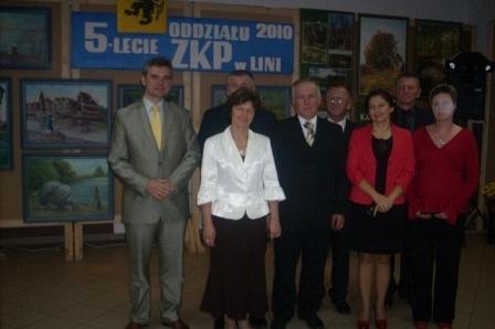 Uczestnicy 5-lecia ZKP Linia pozują na tle okolicznościowego baneru i wystawy.