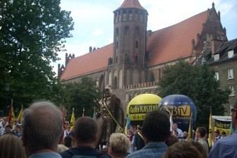 Ludzie zgromadzeni na uroczystości w Gdańsku, w tle zabytkowy budynek z wieżą.