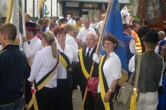 Grupa ludzi w odświętnych strojach z flagą podczas odpustu w Sianowie.