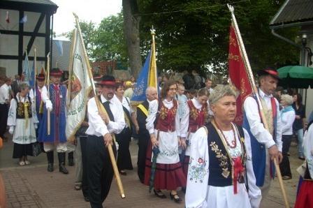 Uczestnicy odpustu w Sianowie w tradycyjnych strojach, niosący sztandary.