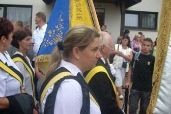 Kobieta z flagą w procesji odpustowej w Sianowie przed budynkiem.
