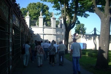 Uczestnicy wycieczki ZKP O/Linia podążają do białego, zabytkowego obiektu pośród drzew.