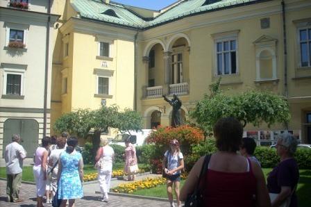 Turyści zwiedzają dziedziniec zabytkowego budynku o zielonym dachu, spacerując w słońcu.
