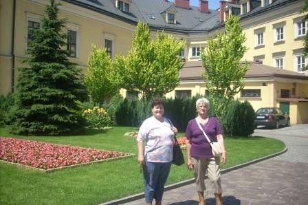 Uczestniczki wycieczki ZKP pozują na tle hotelu lub zabytkowego budynku otoczonego zielenią.