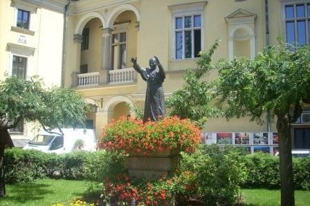 Figura w otoczeniu kwiatów na dziedzińcu historycznego budynku podczas wycieczki.