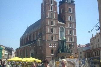 Uczestnicy wycieczki przed Bazyliką Mariacką w Krakowie w słoneczny dzień.