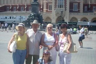 Grupa osób pozuje przed Sukiennicami w Krakowie w słoneczny dzień.