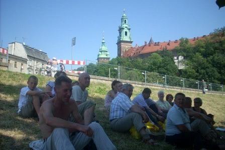 Uczestnicy wycieczki ZKP odpoczywają na trawie z widokiem na Wawel.
