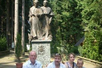 Uczestnicy wycieczki ZKP Linia pozują przed rzeźbą na tle drzew.