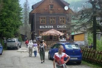 Uczestnicy wycieczki ZKP O/LINIA na ulicy z autami i drewnianym budynkiem.