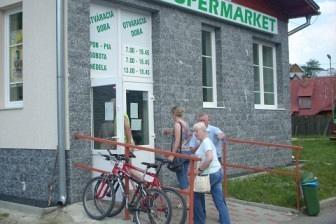 Wycieczkowicze ZKP z rowerem stojący przed małym sklepem spożywczym.