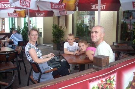Uśmiechnięci uczestnicy wycieczki odpoczywają przy stole pod parasolami.