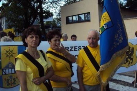Trzy osoby w żółtych strojach z kaszubską flagą na zjeździe.