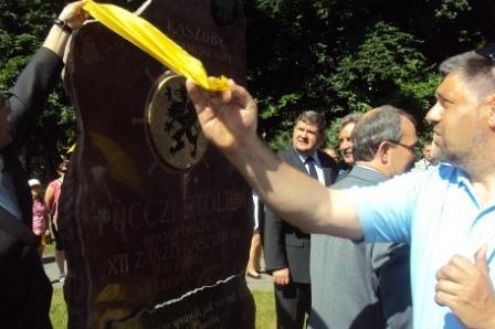 Mężczyzna wręcza żółtą wstęgę podczas uroczystości plenerowej na Zjeździe Kaszubów.