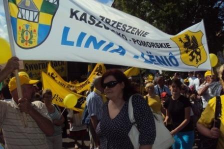 Banner Kaszëbë Gmina Linia nad tłumem ludzi w żółtych strojach podczas zjazdu.