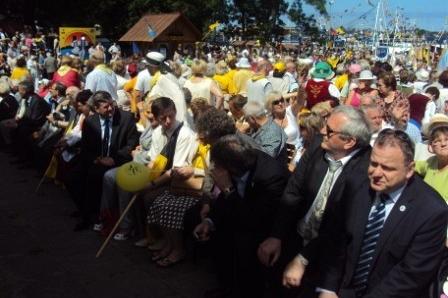 Licznii Kaszubi i uczestnicy zjazdu siedzą i stoją podczas uroczystego zgromadzenia.