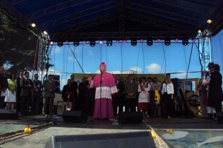 Duchowny w purpurowej szacie przemawia na scenie Zjazdu Kaszubów wśród muzyków.