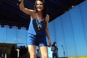 Kobieta z mikrofonem na scenie pozdrawia publiczność podczas Zjazdu Kaszubów.