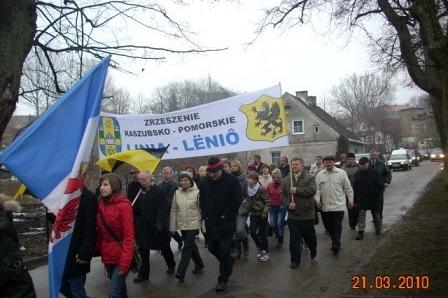Uczestnicy marszu z kaszubską flagą i transparentem podczas Dnia Jedności Kaszubów w Kartuzach.