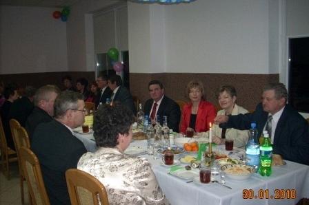 Uczestnicy zabawy karnawałowej siedzą przy suto zastawionym stole w uroczystej atmosferze.