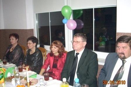 Uczestnicy zabawy karnawałowej siedzą przy stole z balonami w tle.