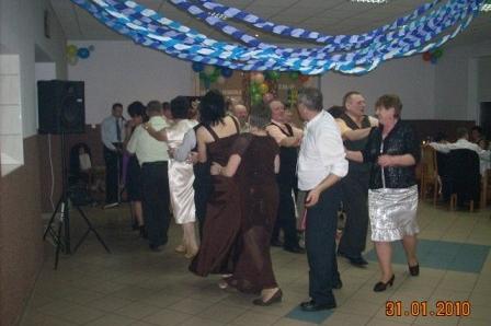 Grupa osób bawi się na zabawie karnawałowej, sala ozdobiona niebieskimi girlandami.