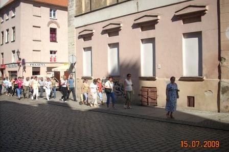 Uczestnicy wycieczki Oddziału w Lini spacerują ulicą w historycznym mieście obok kamienic.
