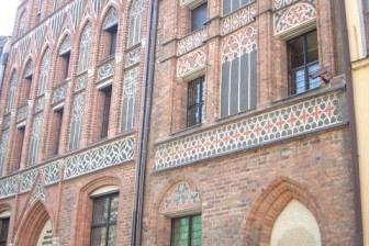 Kamienica w Toruniu z czerwonej cegły, ze zdobionymi szczytami i zielonymi drzwiami.