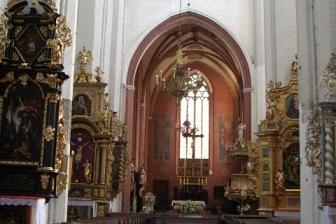 Wnętrze zabytkowego kościoła z długą nawą główną, rzędami ławek i sklepieniami.