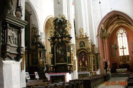 Wnętrze zabytkowej świątyni z rzędami bogato zdobionych ołtarzy i wysokimi arkadami.