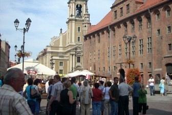 Tłum uczestników wycieczki na rynku Torunia, z ratuszem w tle.