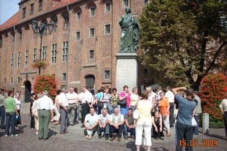 Członkowie Zrzeszenia Kaszubsko-Pomorskiego stoją przy pomniku i zabytkowym budynku.