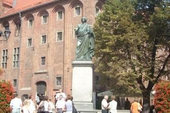 Grupa wycieczkowiczów przed zabytkowym kościołem z wieżą i pomnikiem na placu.