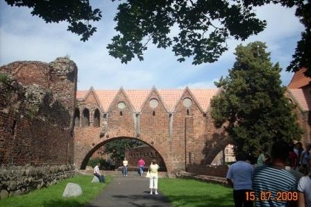 Uczestnicy wycieczki oglądają romańską architekturę w Strzelnie, ceglane mury i łuk.