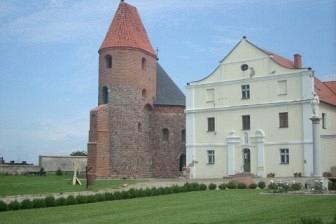 Poklasztorny zespół z romańską rotundą w Strzelnie i białą fasadą budynku.