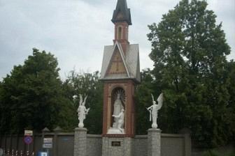 Kalwaria w Licheniu z figurami świętych i krzyżem na tle drzew, pochmurny dzień.